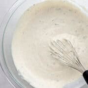 Close up overhead view of combined dressing ingredients in glass mixing bowl with whisk.