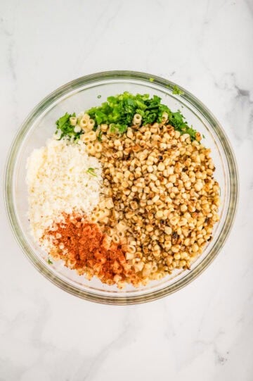 Pasta salad ingredients added to large glass mixing bowl.