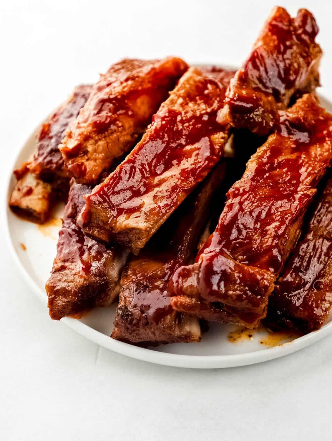 Close up front view of ribs stacked on white plate. 