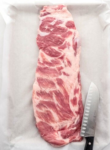 Overhead view of ribs on parchment lined sheet pan by a knife.