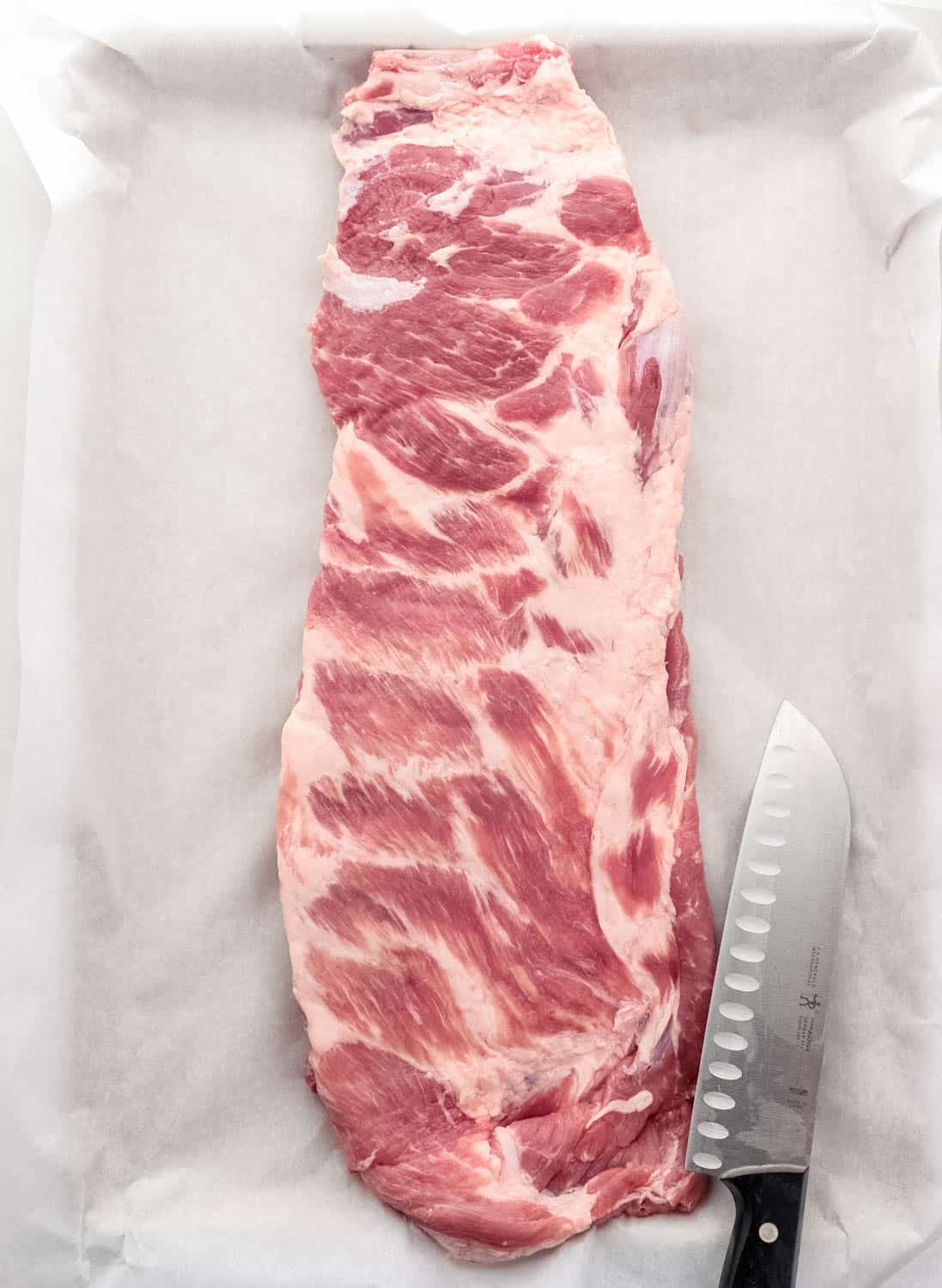 Overhead view of rack on rib on parchment lined sheet pan by a knife. 