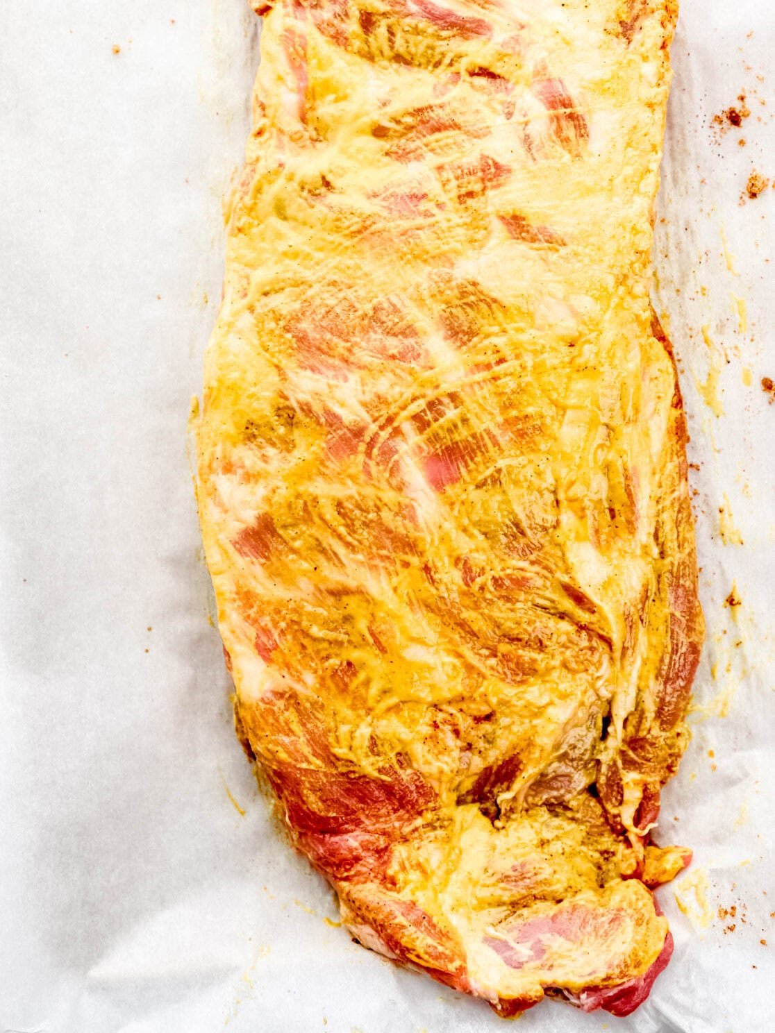 Ribs coated with mustard on parchment paper. 