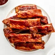 Overhead view of finished ribs stacked on white plate on white surface.