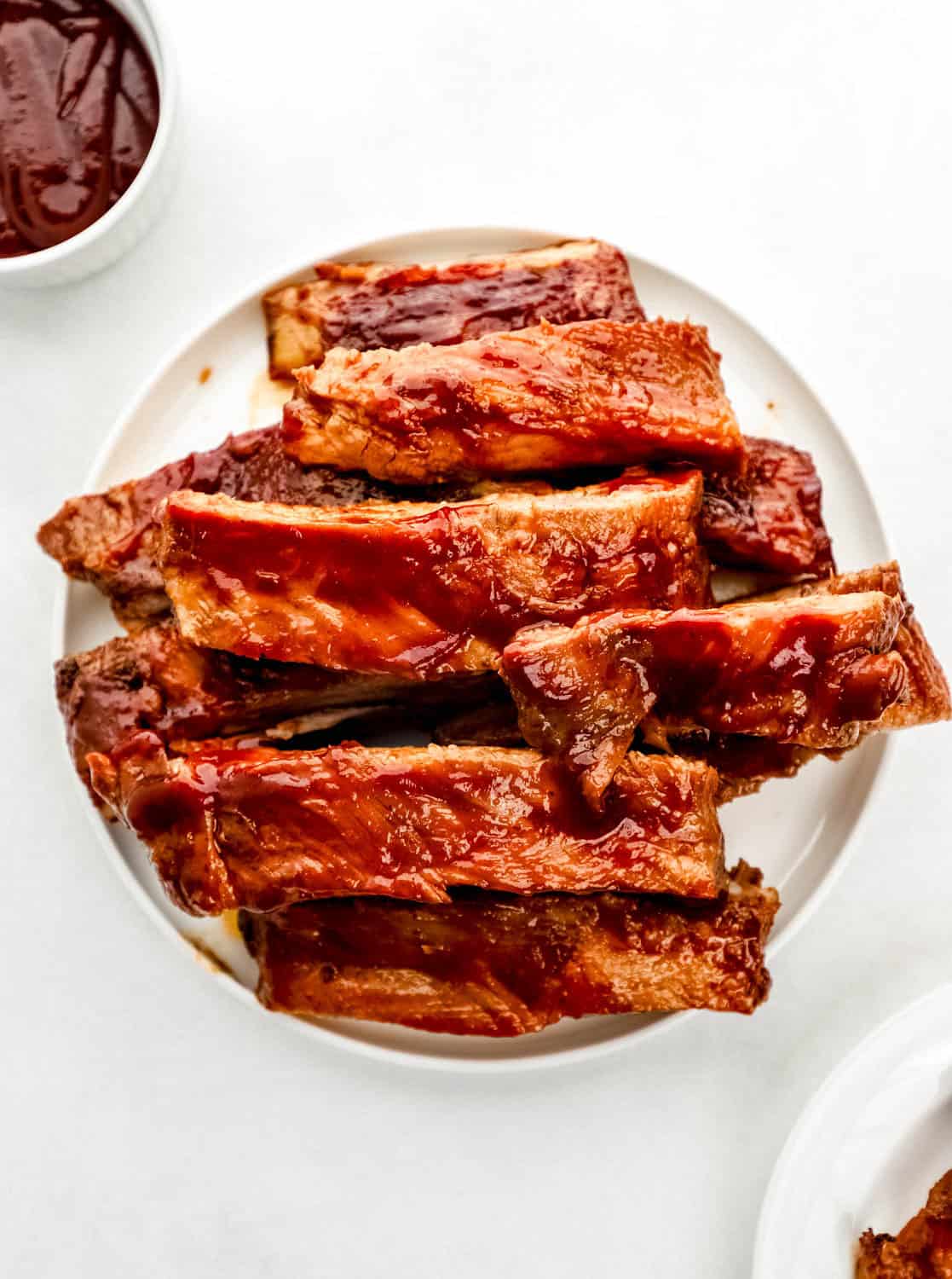 Overhead view of ribs on a white plate by a small bowl of sauce.