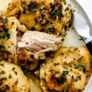 Overhead view of baked chicken on white plate with a knife on it.