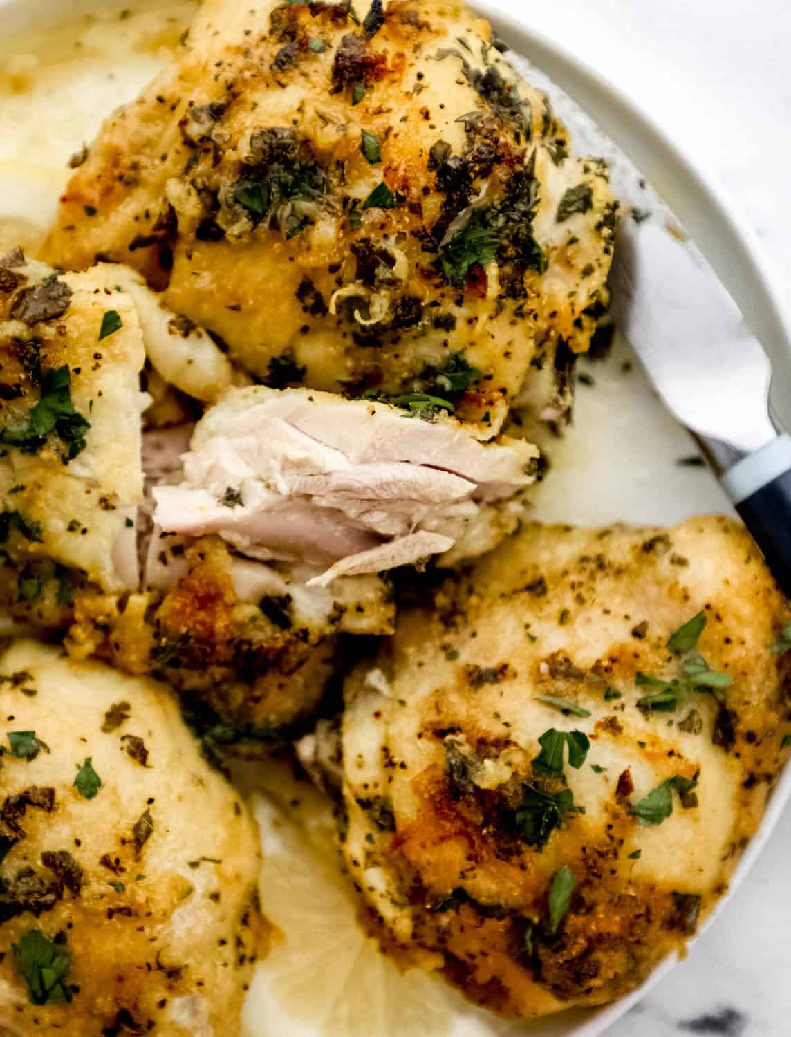 Close up overhead view of baked chicken on white plate with a knife. 