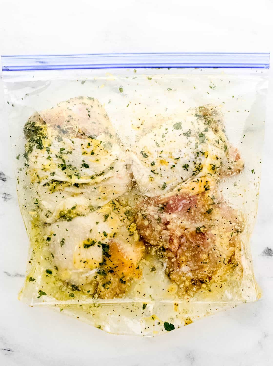 Marinating chicken thighs in a plastic storage bag on marble surface. 