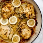 Overhead view of finished chicken thighs in braiser pan on marble surface.