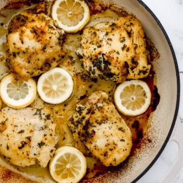 Overhead view of finished chicken thighs in braiser pan on marble surface.