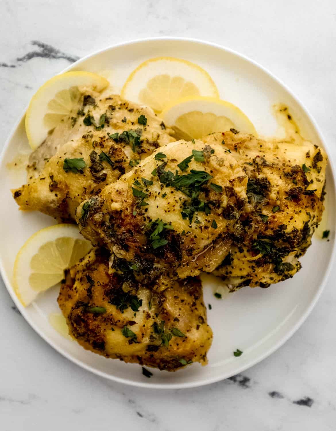 Overhead view of finished chicken stacked on white plate with lemon slices. 
