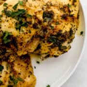 Close up view of chicken thighs on white plate topped with parsley.