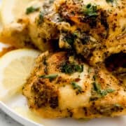 Close up side view of chicken on white plate with lemon slices.