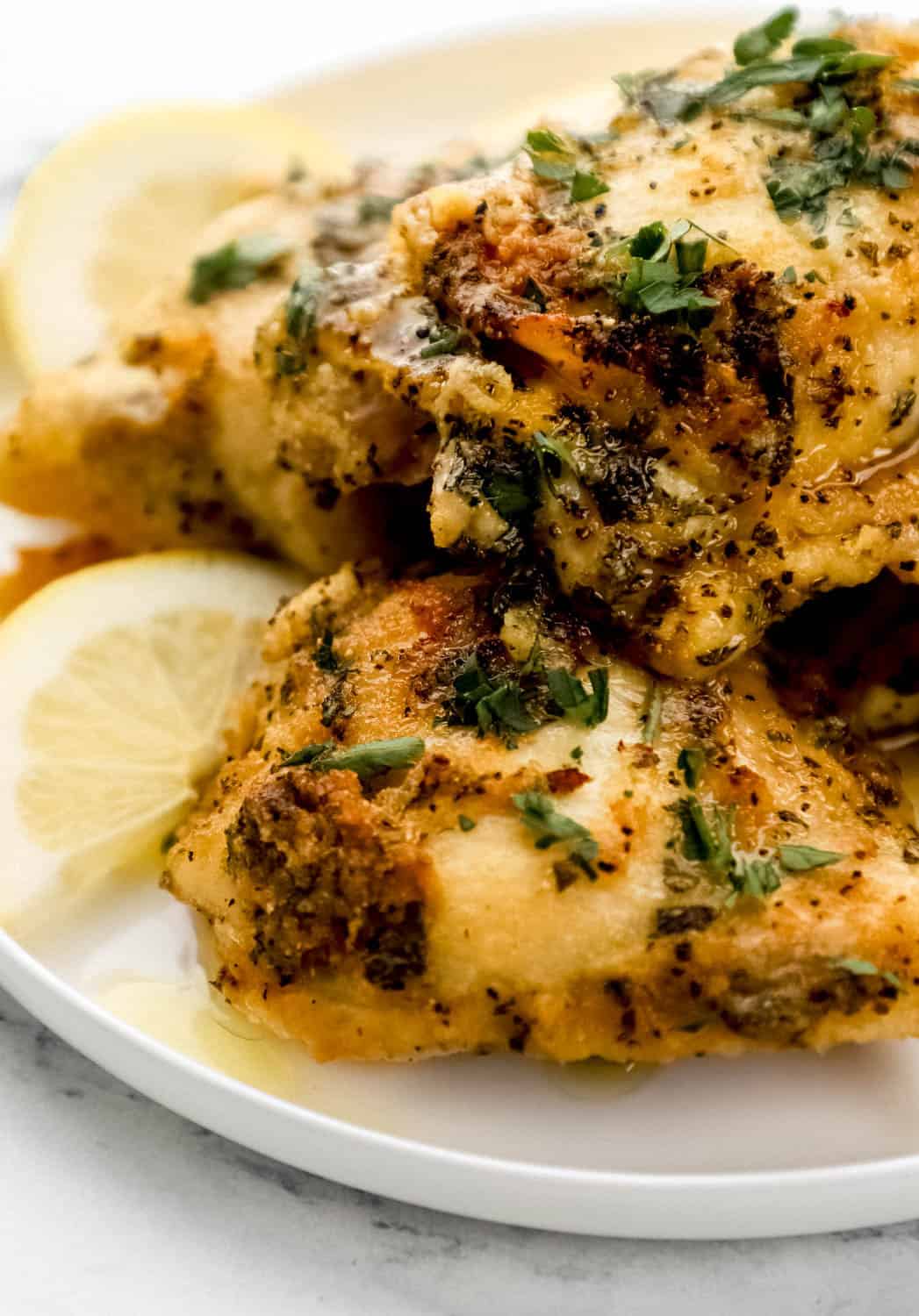 Close up side view of baked chicken and lemon slices on a white plate. 