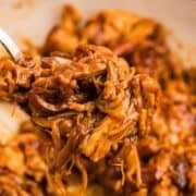 Close up view of fork over dutch oven with pulled chicken on it.