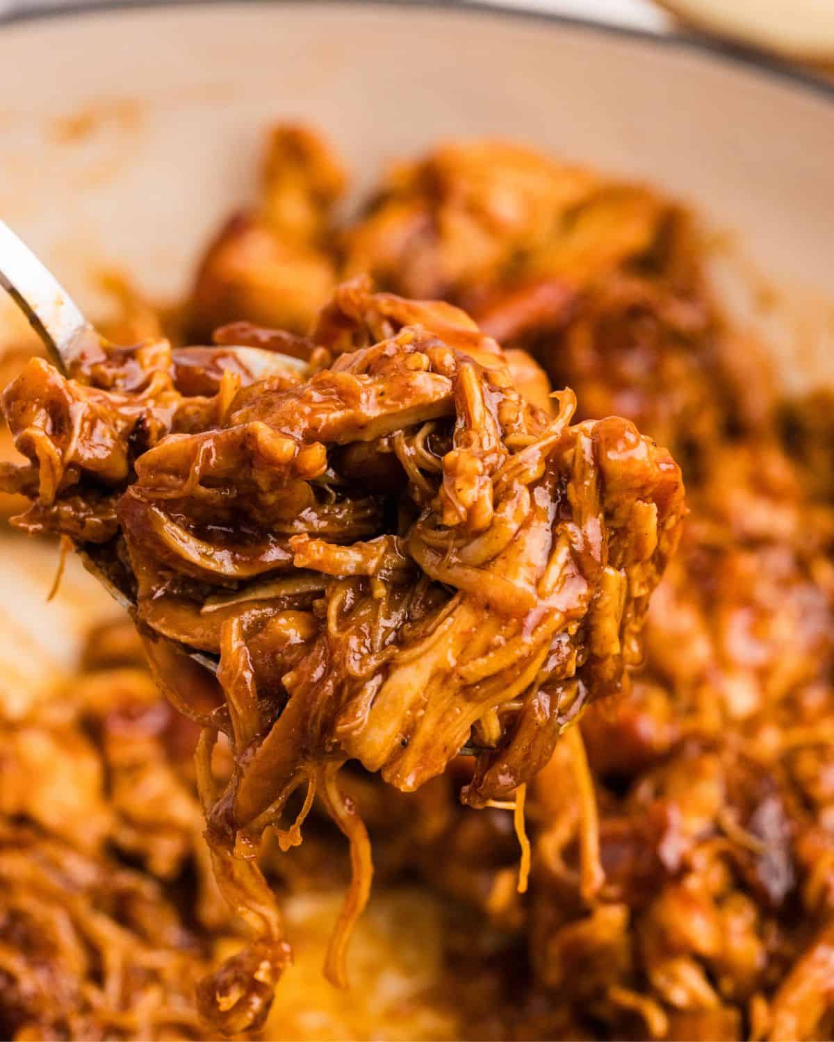 Close up view of fork with pulled chicken on it held over the pot with the rest of the finished chicken. 