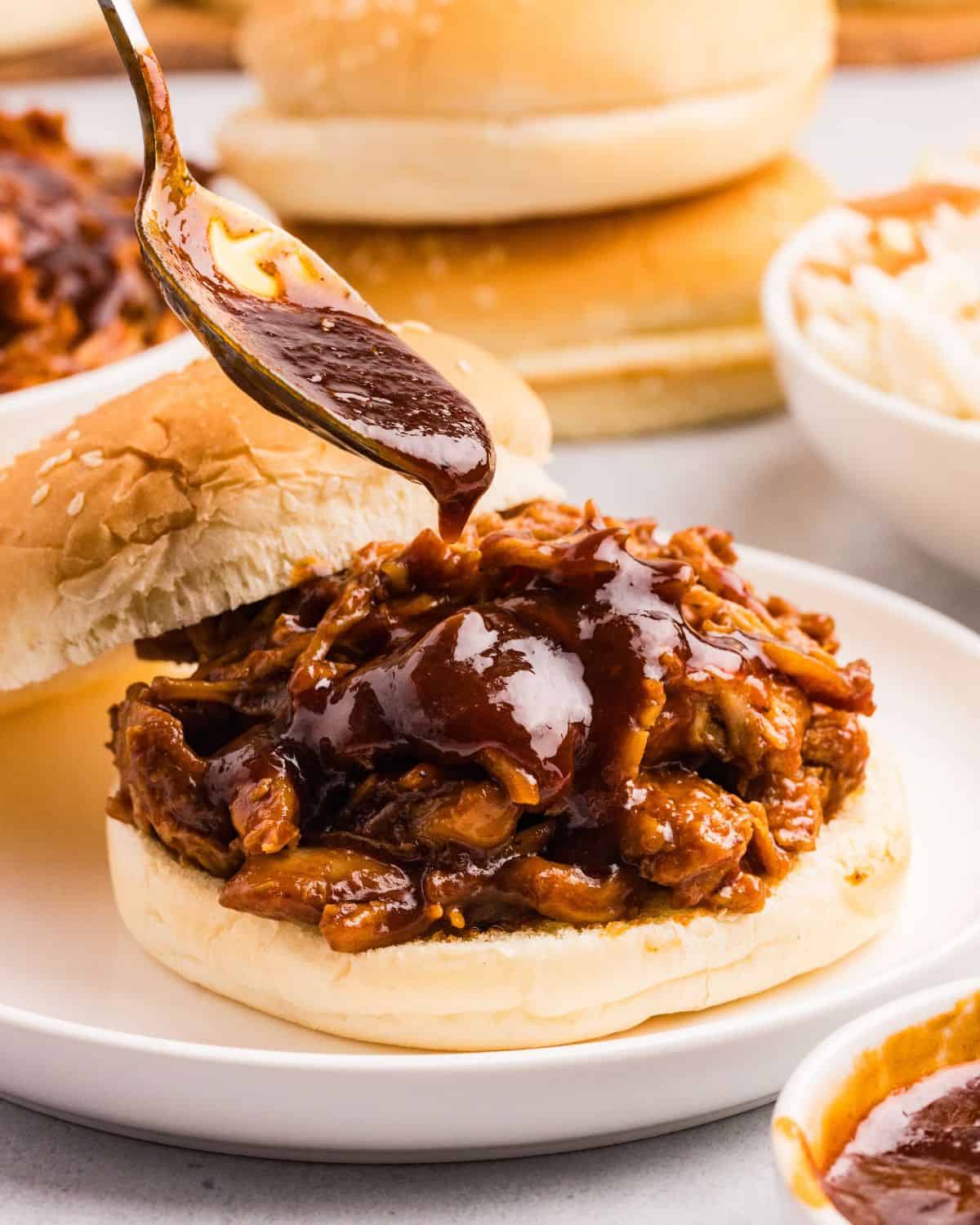 Close up view of barbecue chicken on bun with spoon adding sauce to it. 
