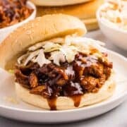 Close up view of barbecue pulled chicken sandwich topped with coleslaw on white plate.