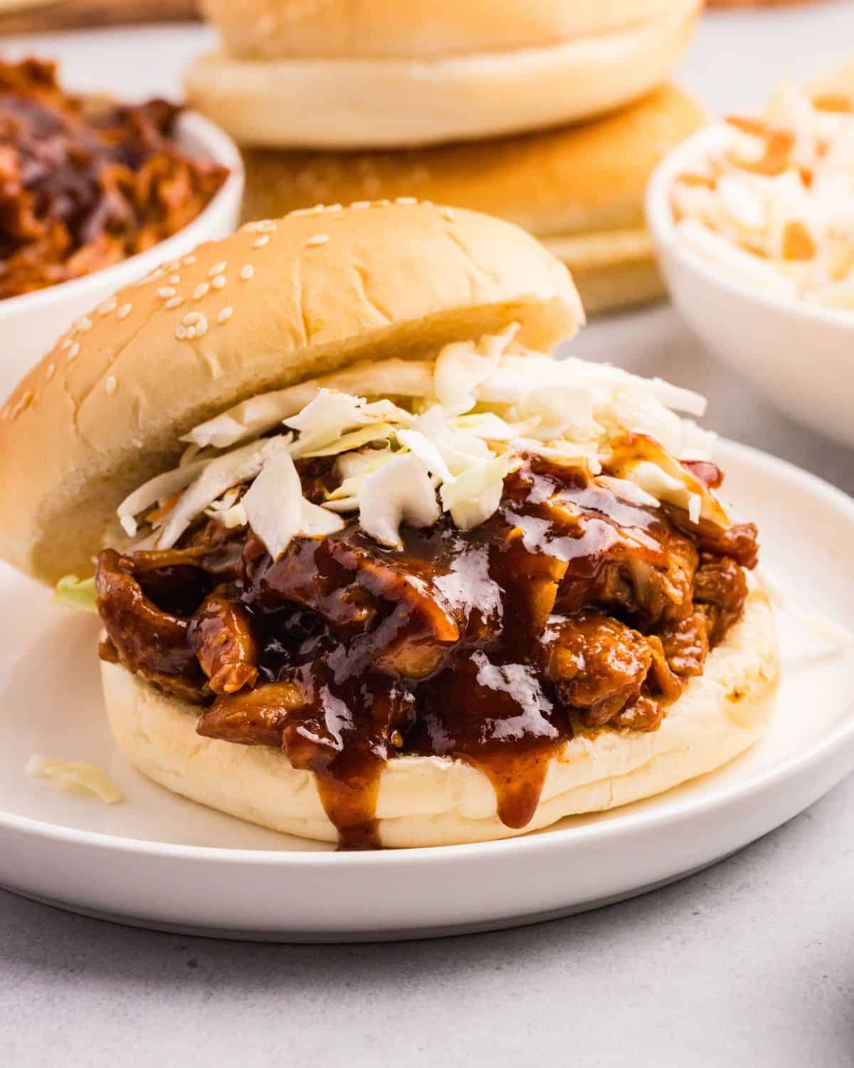 Close up view of barbecue chicken on bun topped with coleslaw on white plate. 