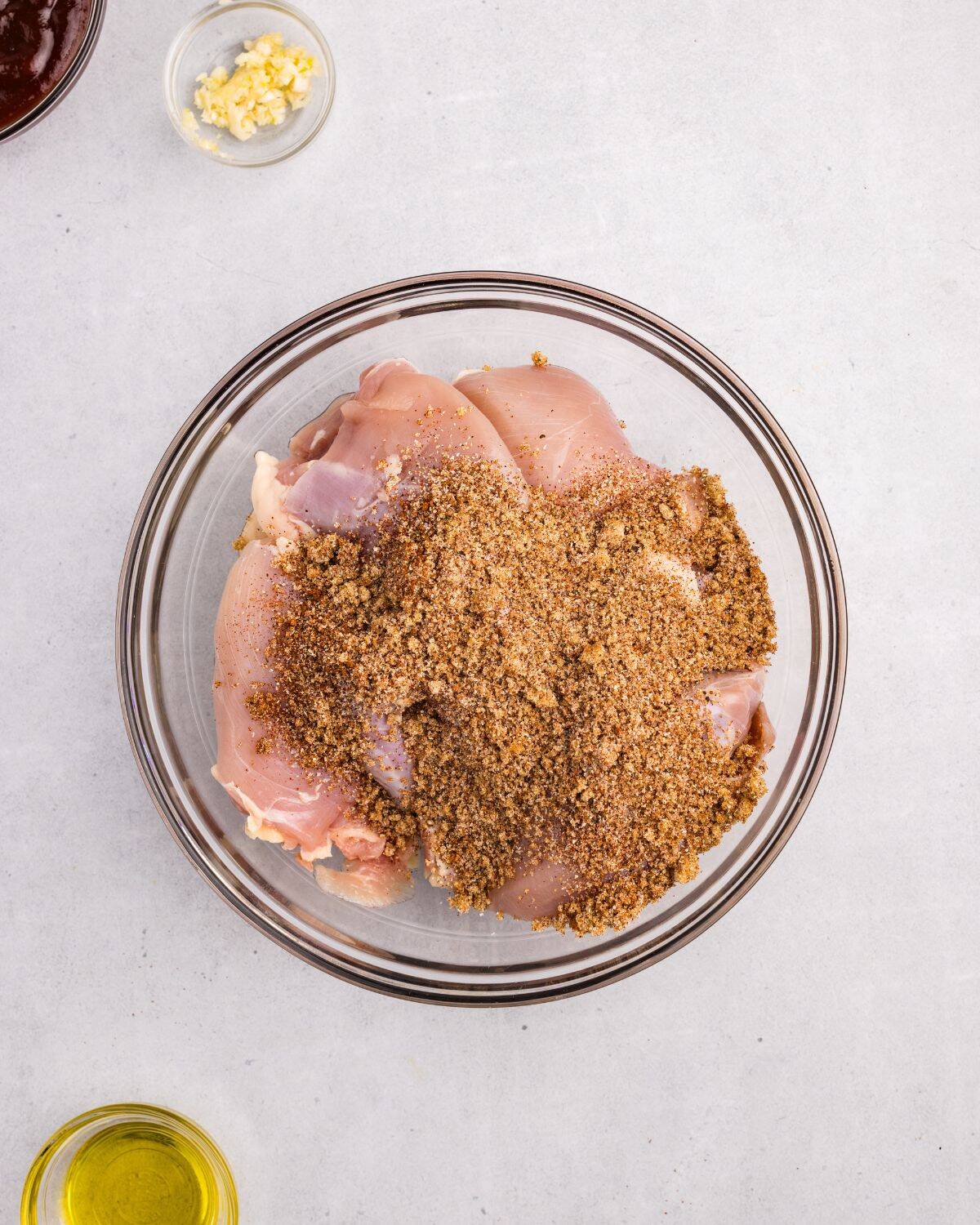 Overhead view of chicken thighs topped with seasoning blend in large glass bowl. 