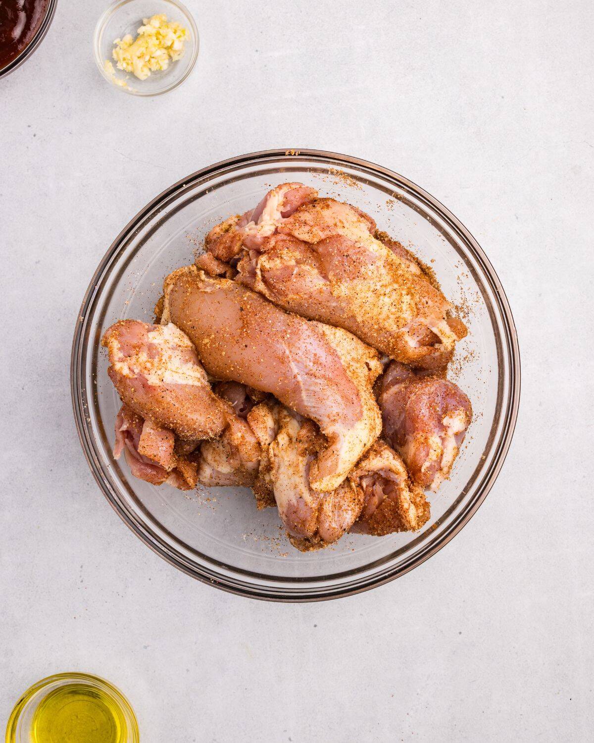 Overhead view of seasoned chicken in large glass bowl. 
