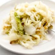 Close up side view of serving of cabbage on white plate with fork in it.