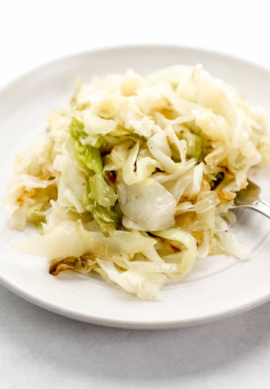 Close up side view of serving of cabbage on white plate with fork in it. 