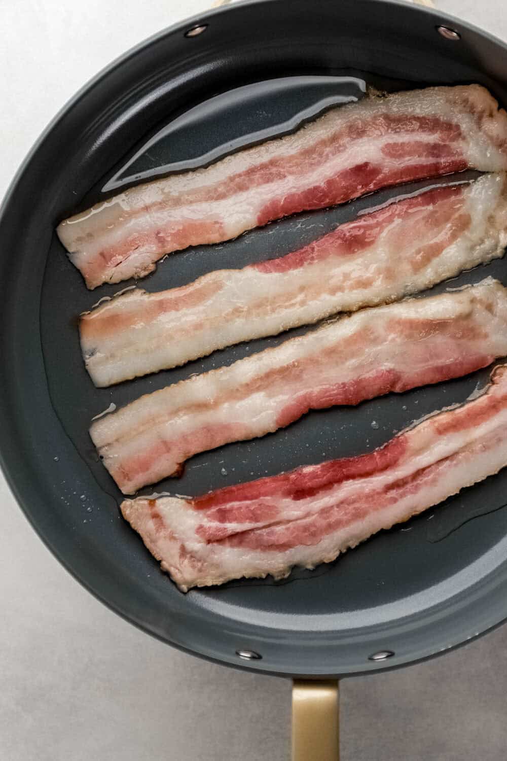 Four slices of bacon cooking in a skillet. 