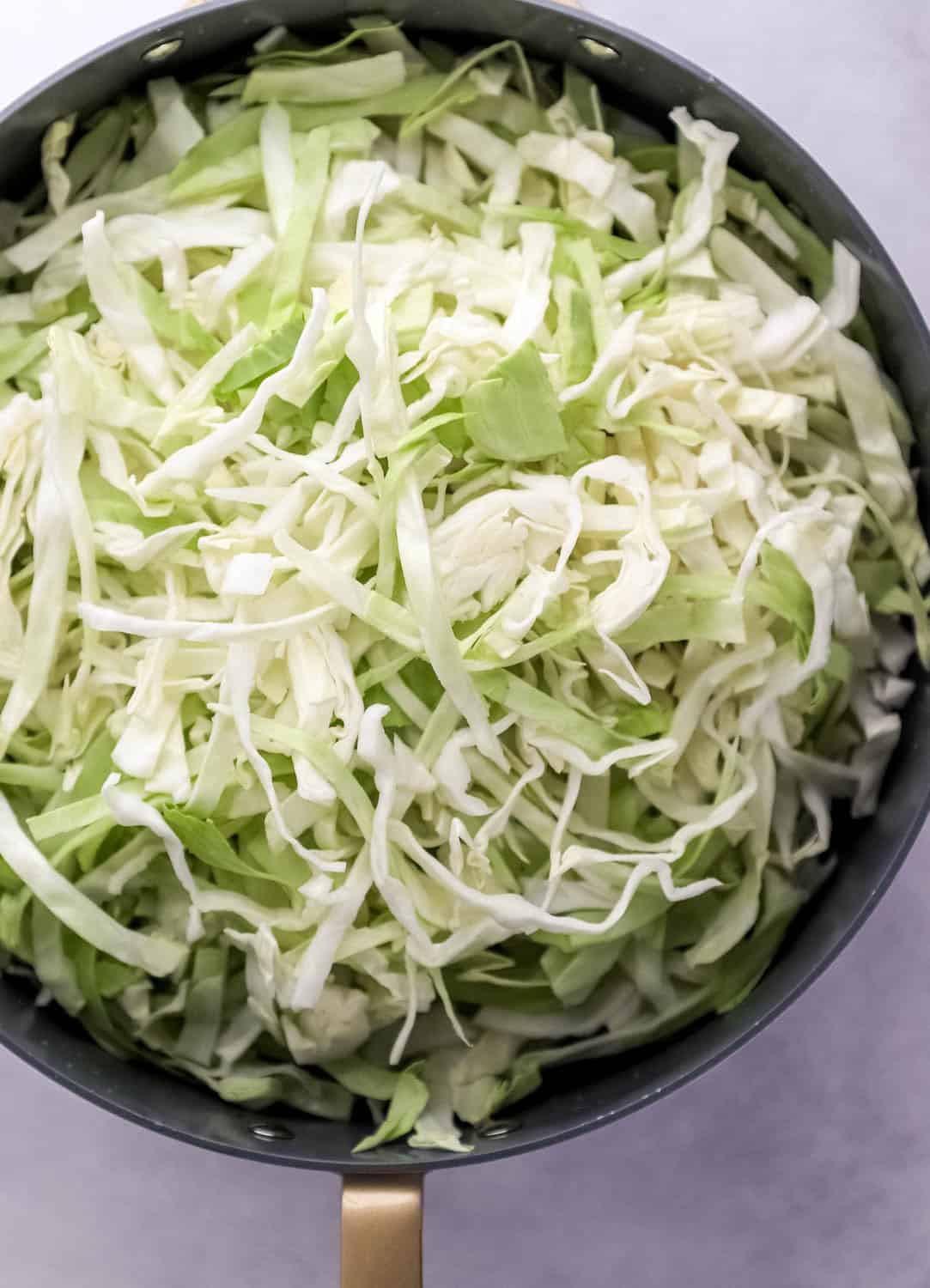 Overhead view of shredded cabbage added to large skillet with oil in it. 