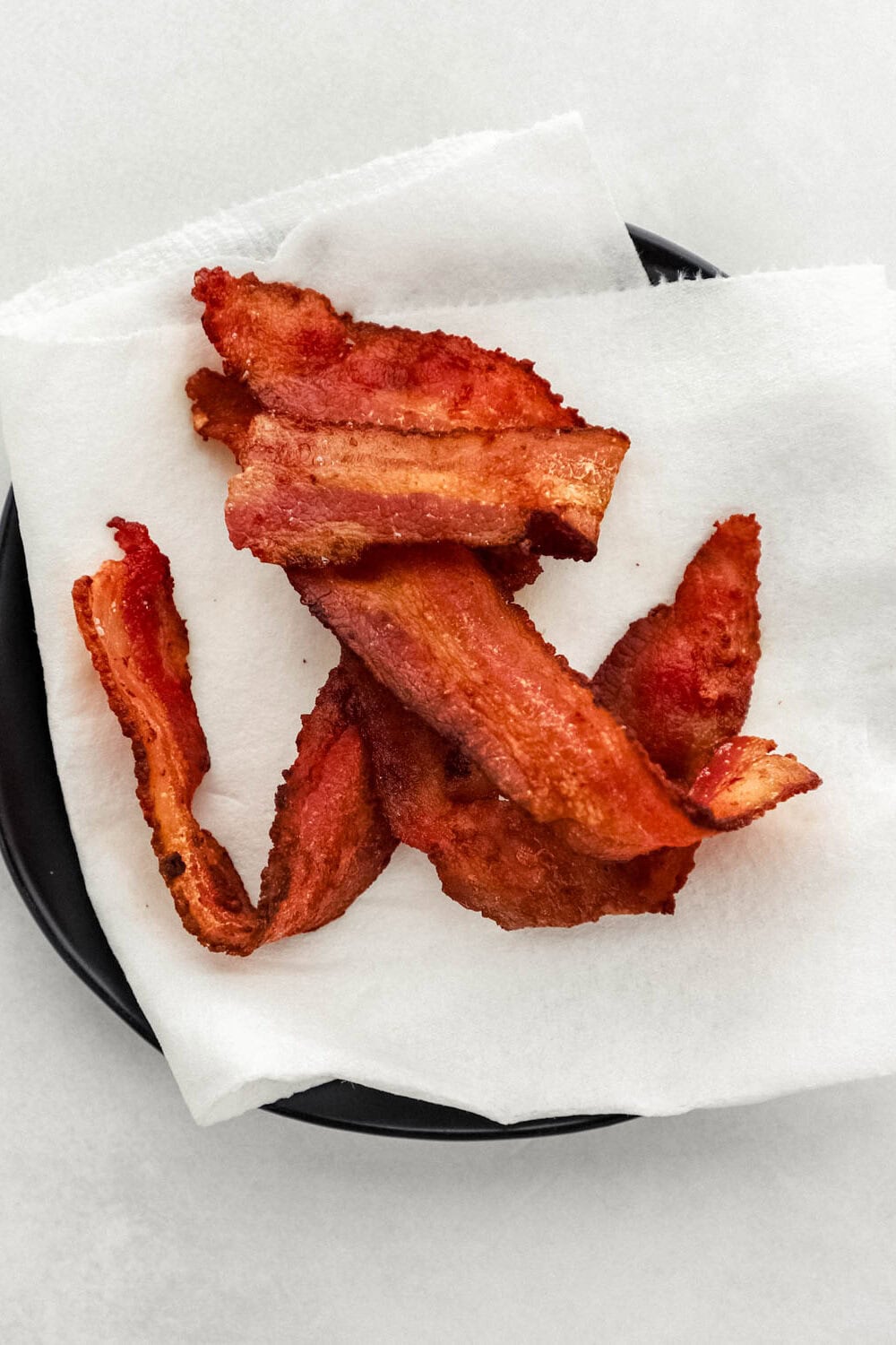 Cooked bacon on paper towel lined small black plate. 