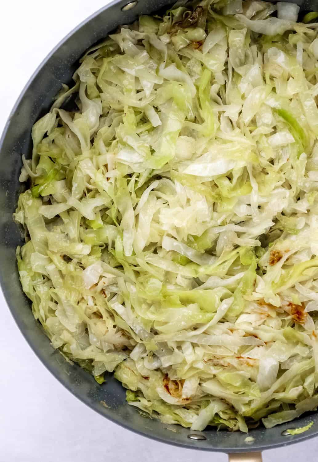 Overhead view of finished cabbage in large skillet on grey surface. 