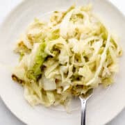 Overhead view of serving of cabbage on white plate with fork in it.