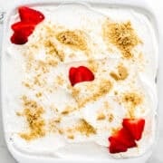 Overhead view of finished strawberry delight in white baking dish on marble surface.
