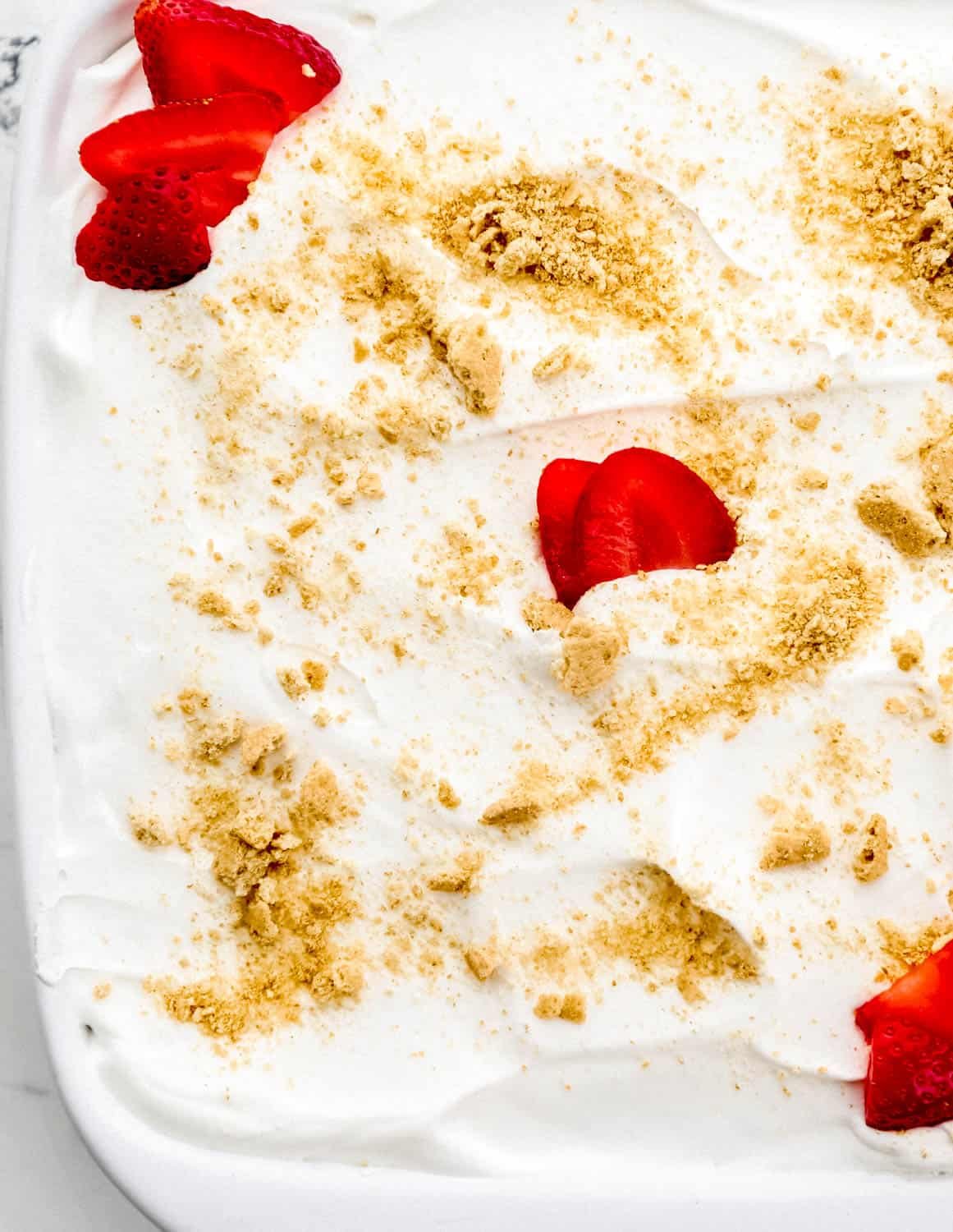 Overhead view of finished dessert in white baking dish topped with graham cracker crumbs and sliced strawberries. 