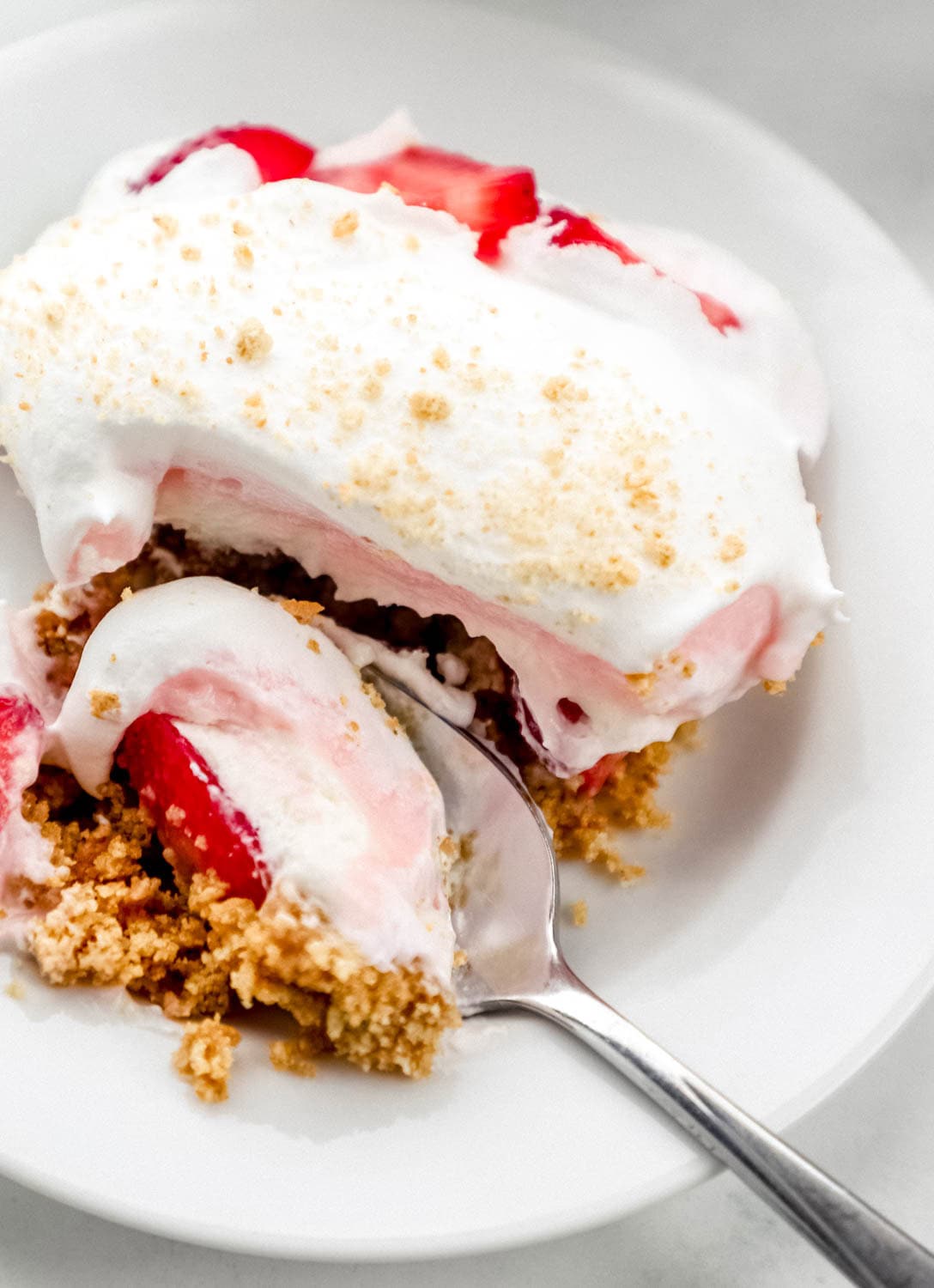 Single serving of finished strawberry delight on white plate with spoon in it. 