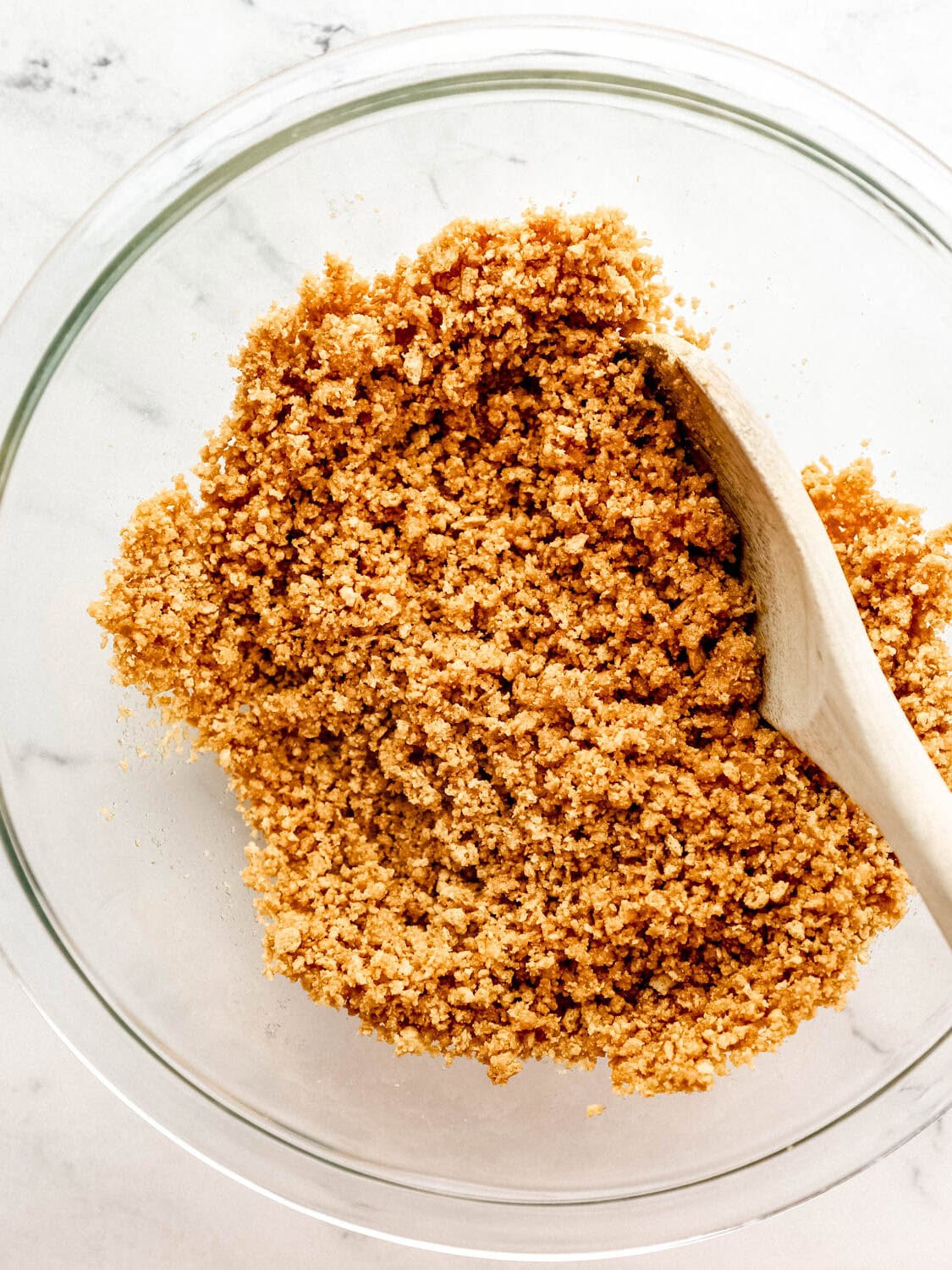 Crust ingredients combined in large glass mixing bowl with wooden spoon. 