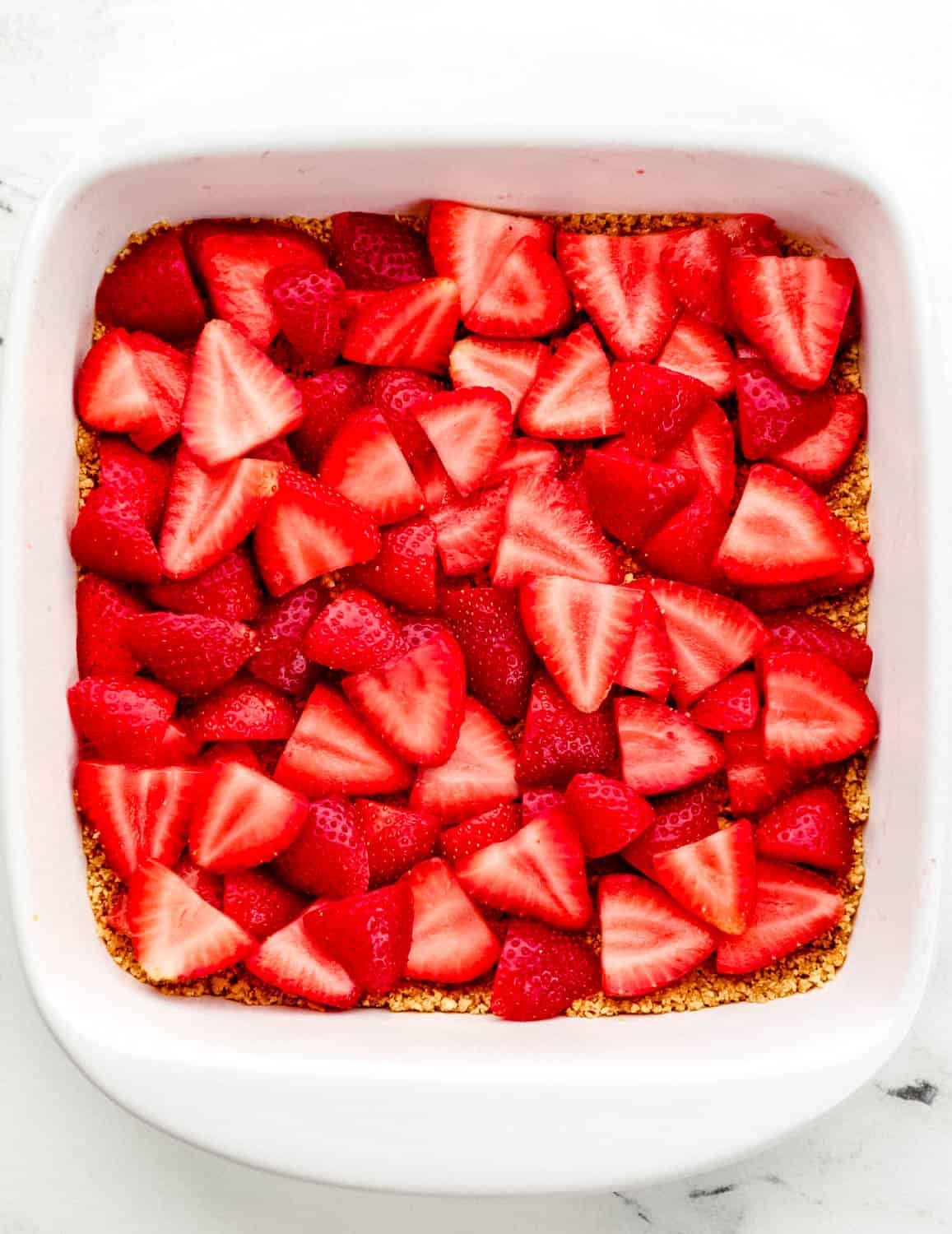 Overhead view of sliced strawberries added to the top of the crust. 