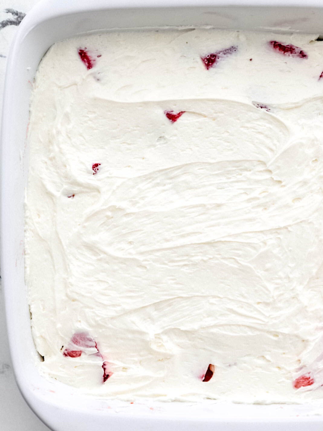 Cream cheese layer added to the other layers in a white square baking dish. 