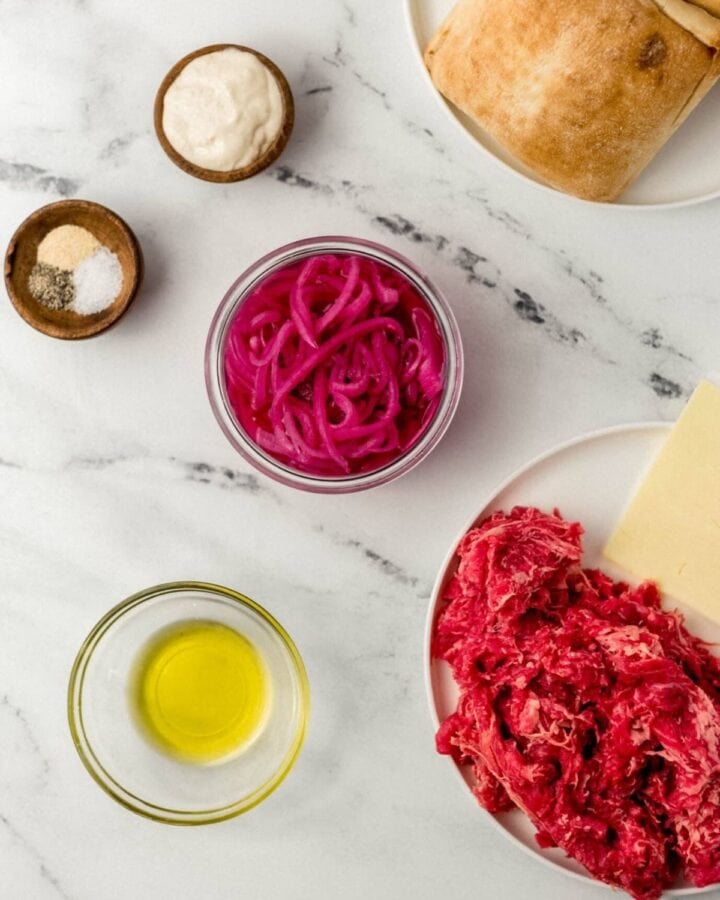 Ingredients needed to make sandwich in separate bowls on marble surface. 