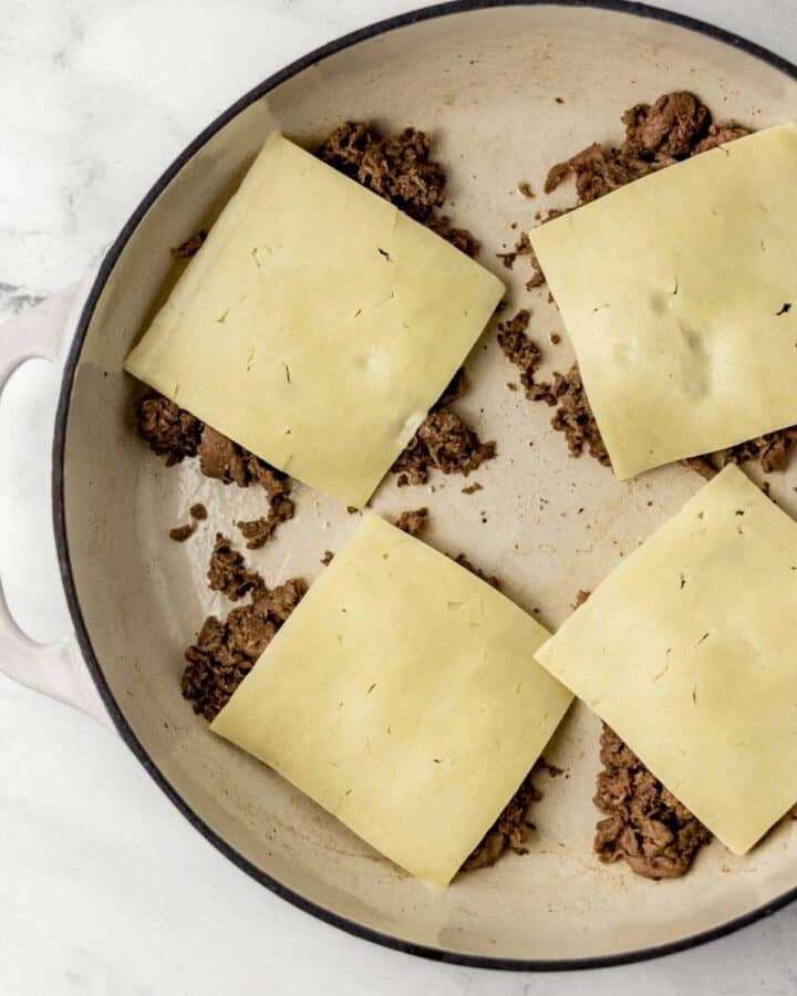 Cooked steak in pan topped with sliced cheese. 