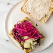 Sandwich being assembled on white plate on top of marble surface.