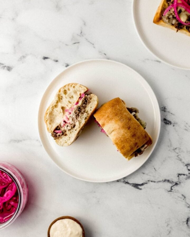 Overhead view of steak sandwich cut in half on white plate on marble surface. 