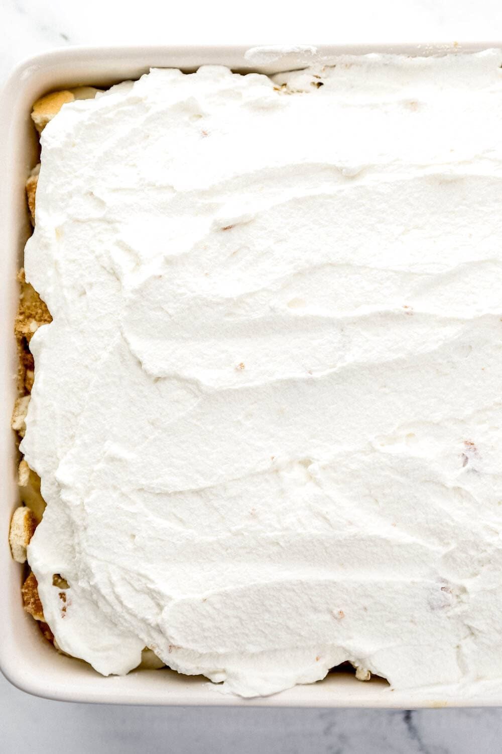 Whipped topping added on top of the banana slices and cake in baking dish.