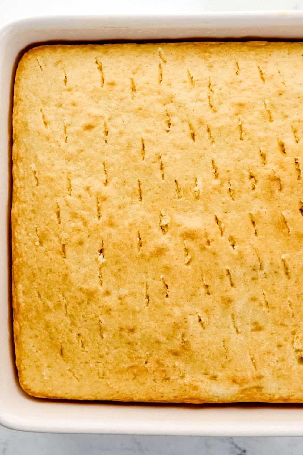 Overhead view of cake in baking dish with holes poked into it.