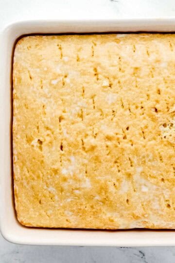 Milk mixture poured onto baked cake with holes poked in it.