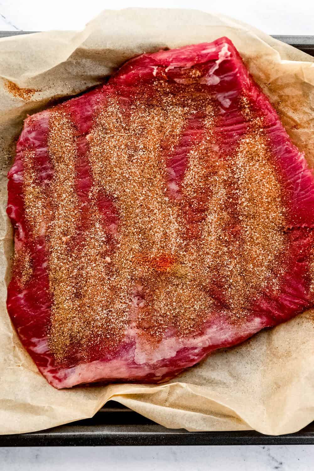 Overhead view of seasoned steak on parchment lined sheet pan.