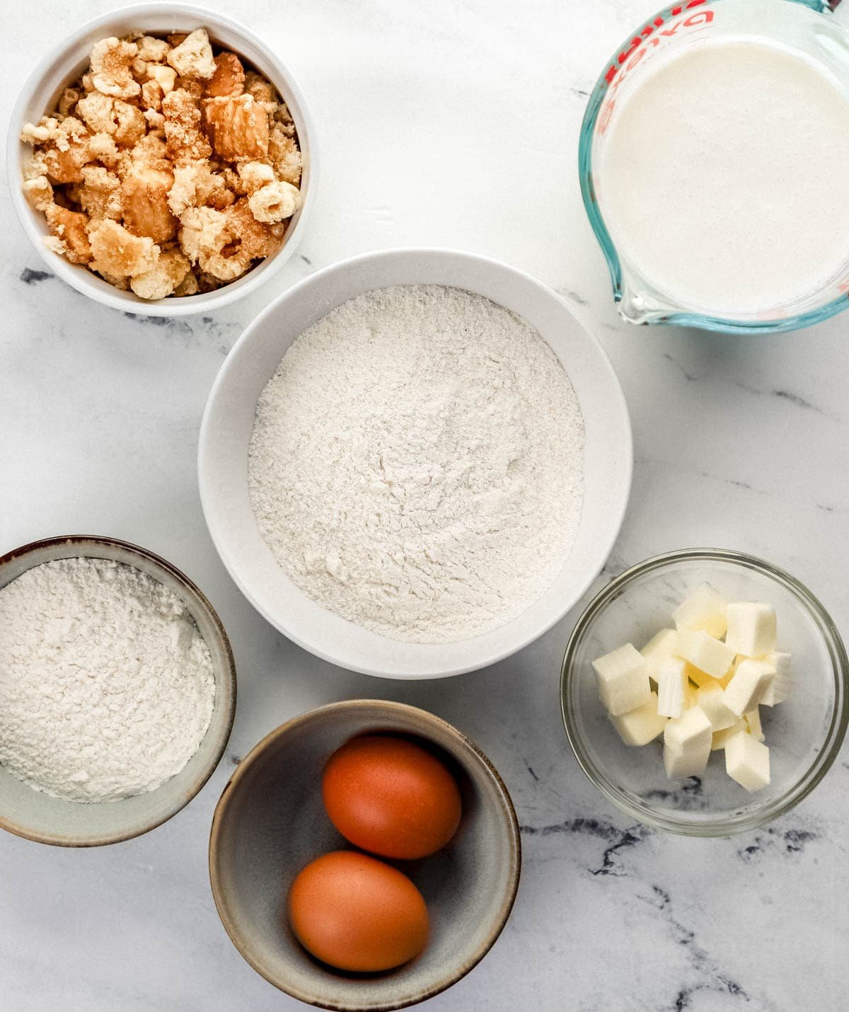 Overhead view of ingredients to make cornbread in separate bowls on marble surface. 