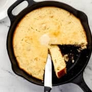 Overhead view of cornbread in a cast iron skillet with a knife in it.