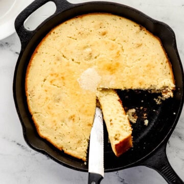 Overhead view of cornbread in a cast iron skillet with a knife in it.