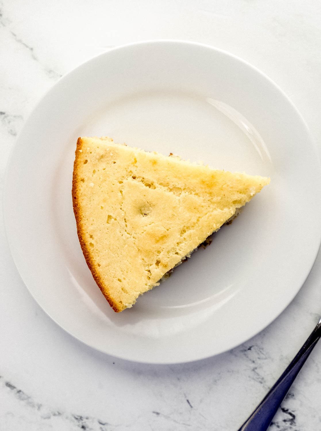 Overhead view of slice of cornbread on a white plate by a fork. 