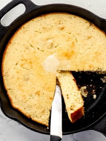 Overhead view of finished cornbread in cast iron skillet with a knife in it.